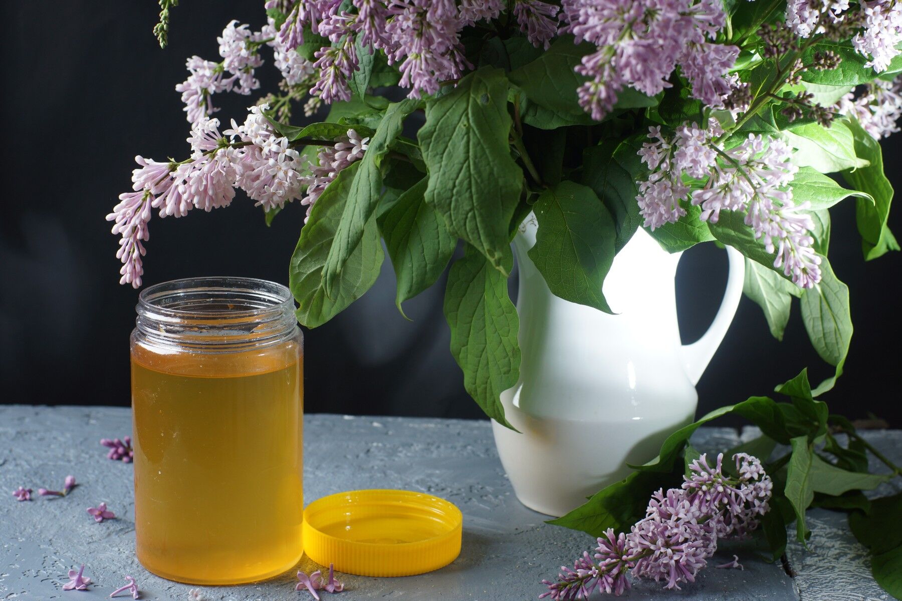 Lilac blooms in a jug next to a jar of honey
