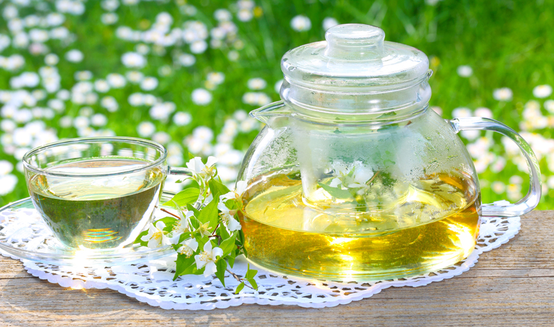tea in a carafe with cup and cut flowers beside it