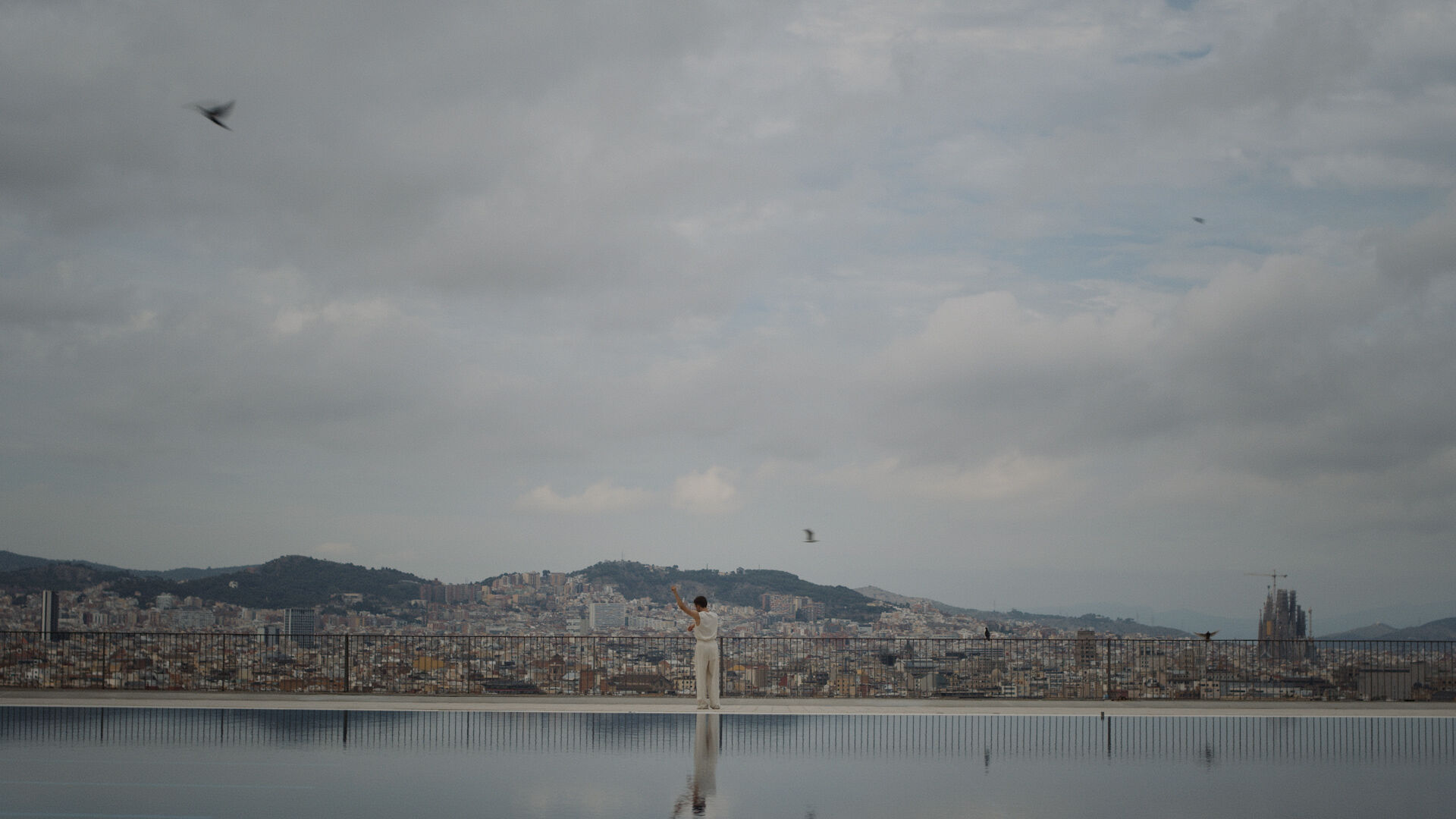 A man on a rooftop, dressed in white, looking out over a city