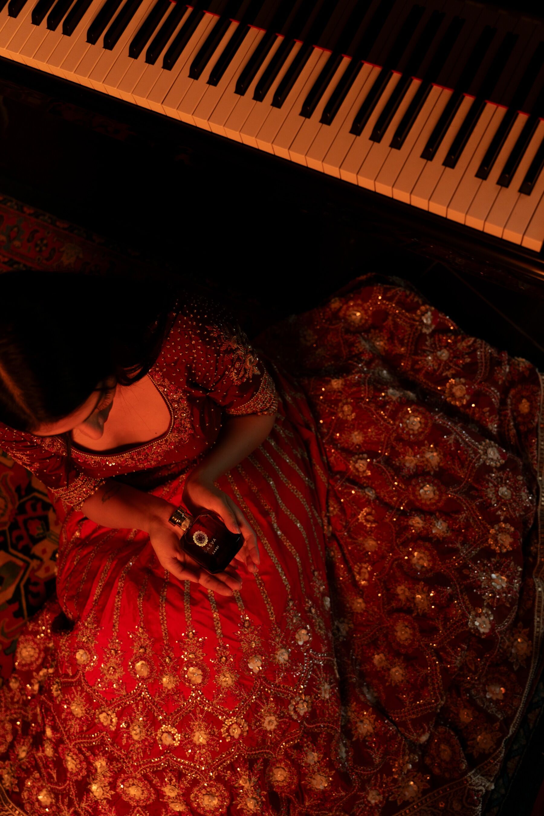 A woman and a piano viewed from above. The woman is holding a bottle of perfume