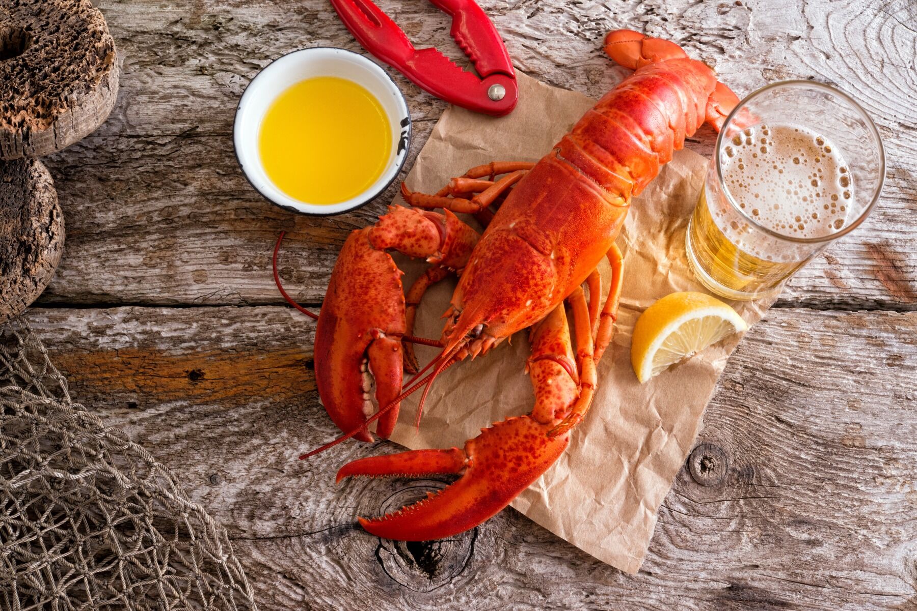A pink lobster on a wooden board surrounded by butter and crackers