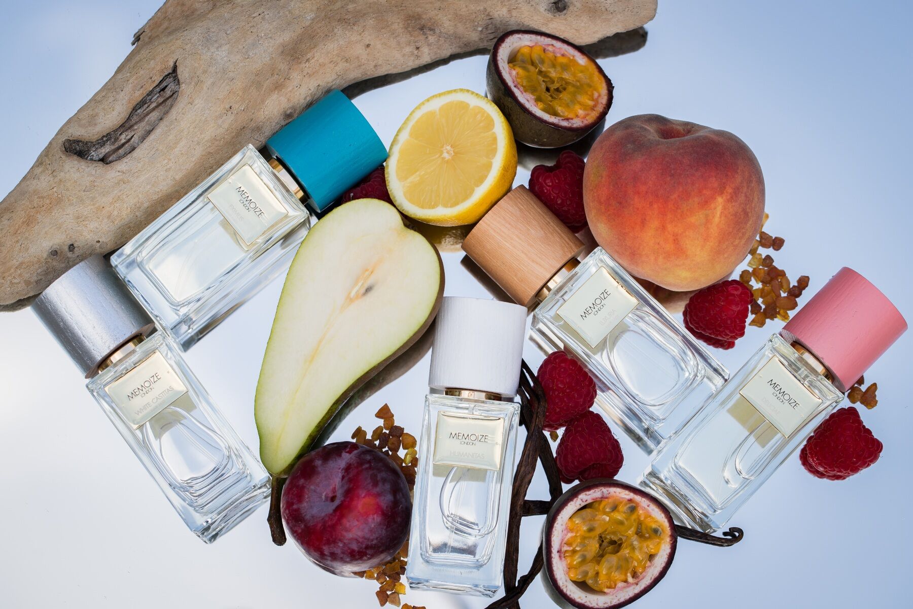 A flat lay of fragrances and fruits on a white background with some woody branches