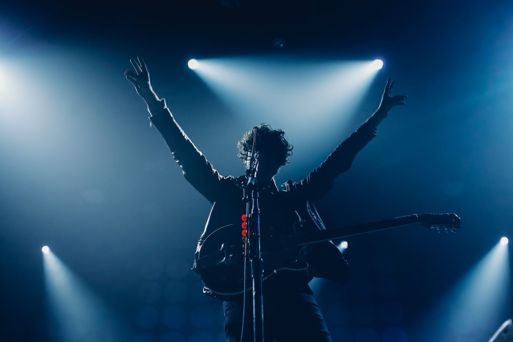 A rockstar silhouetted on stage with bright lights behind, he is holding a guitar