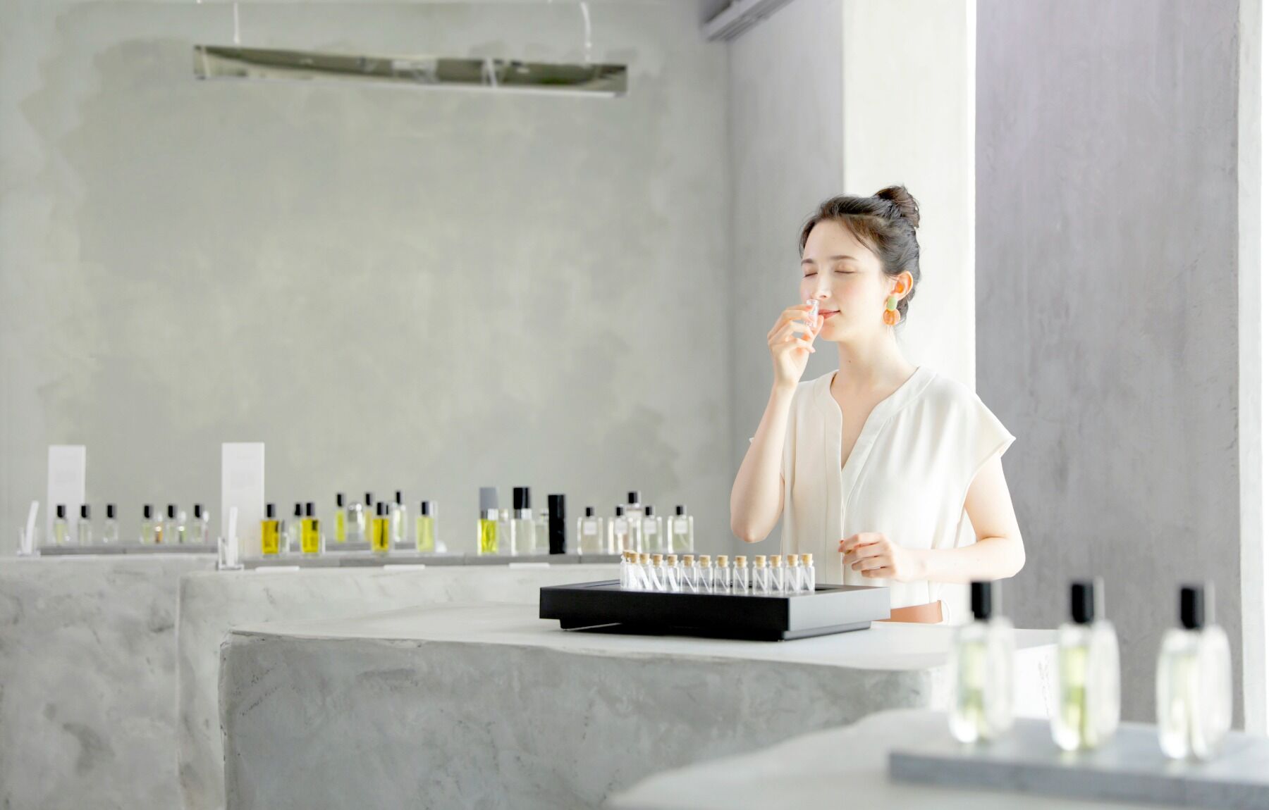 A woman sniffing perfume in a white concrete store