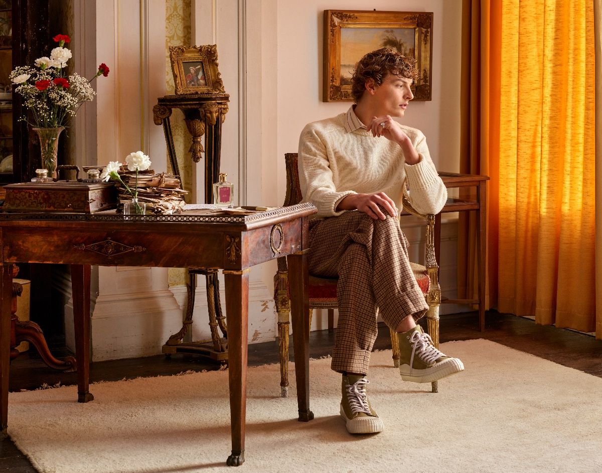 A handsome young man sat at an antique desk bathed in orange light and staring wistfully into the distance