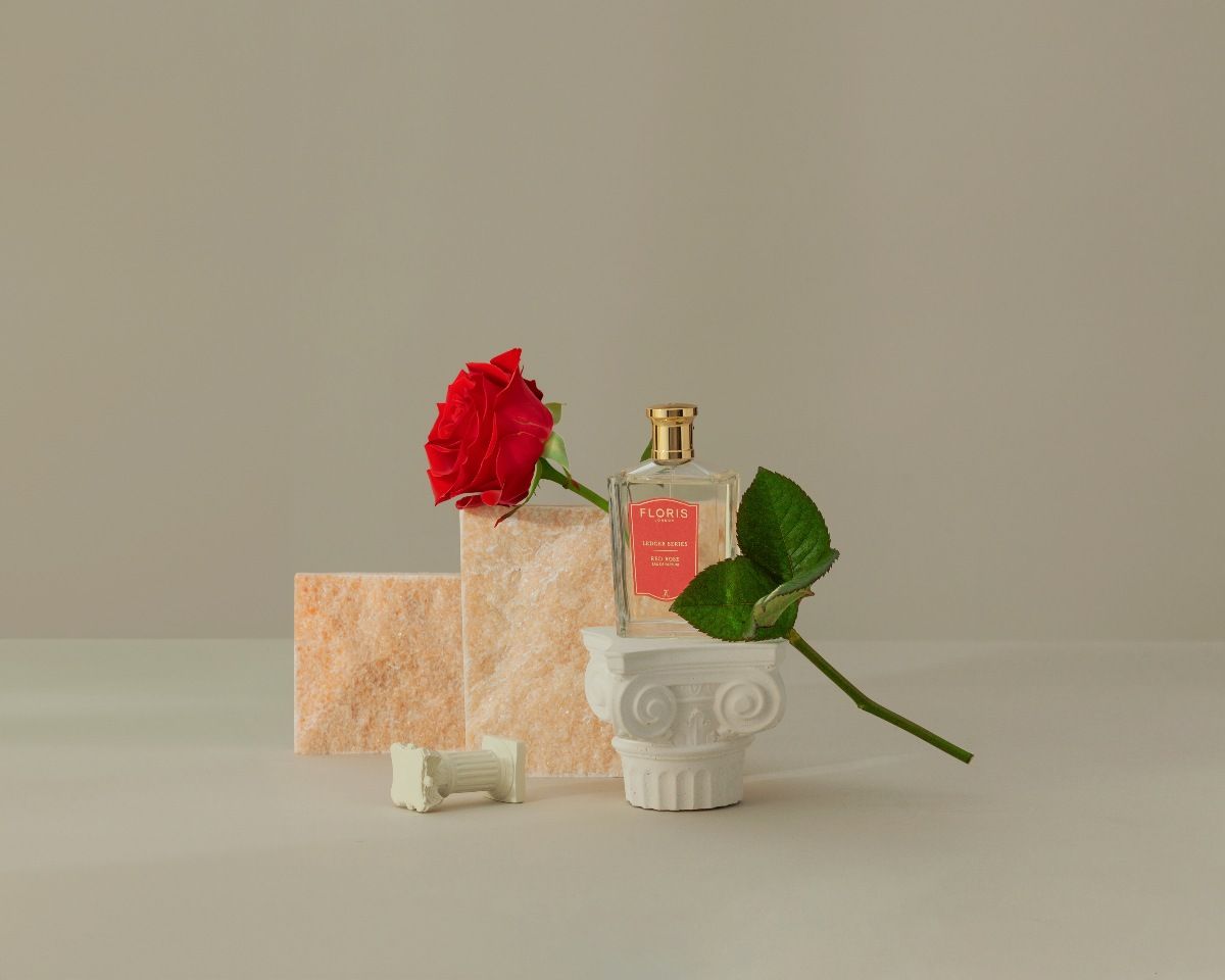 The Floris fragrance Red Rose on a beige background shown with a red rose