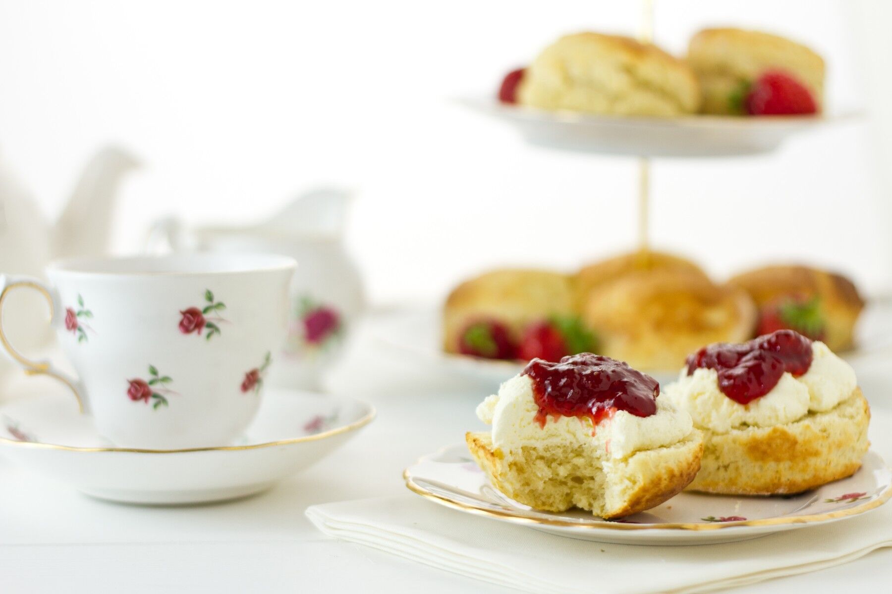 Scones with jam and cream and a teacup set on a white tablecloth