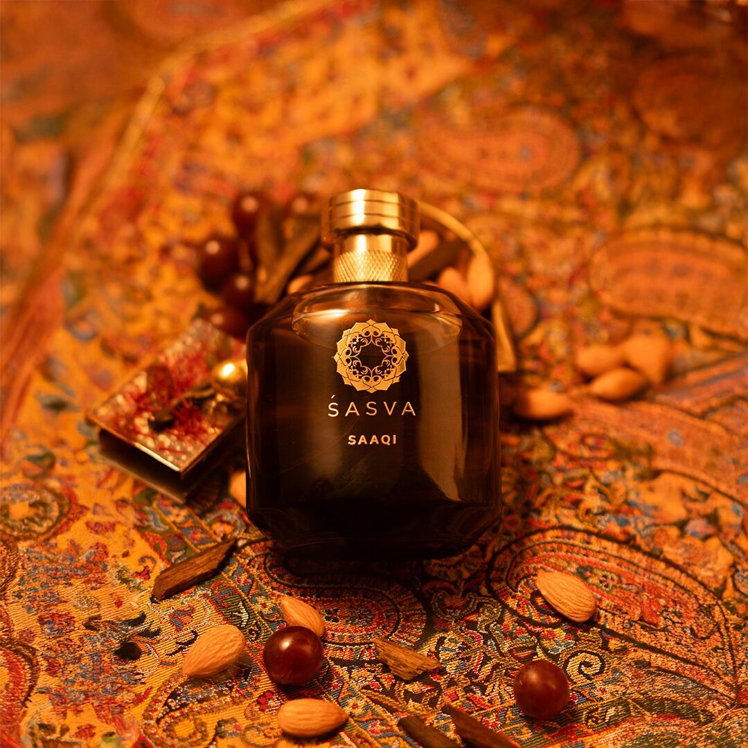 Saaqi set on an orange and red toned backdrop of richly pattered Indian fabric