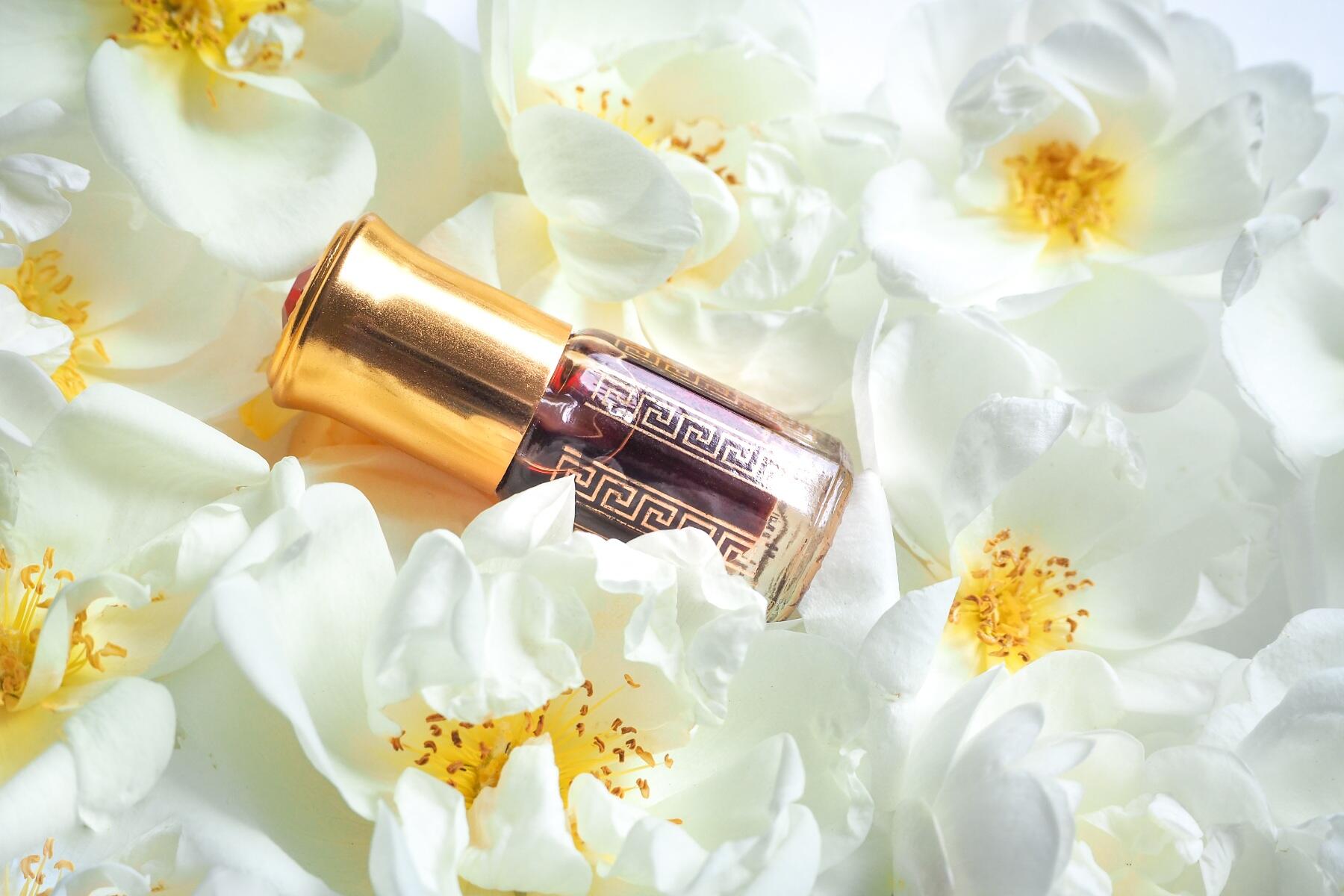 A vial of oud laid on a bed of white roses