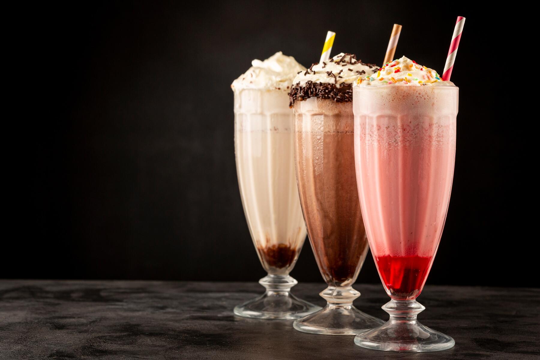 Three milkshakes with straws stood against a black backdrop