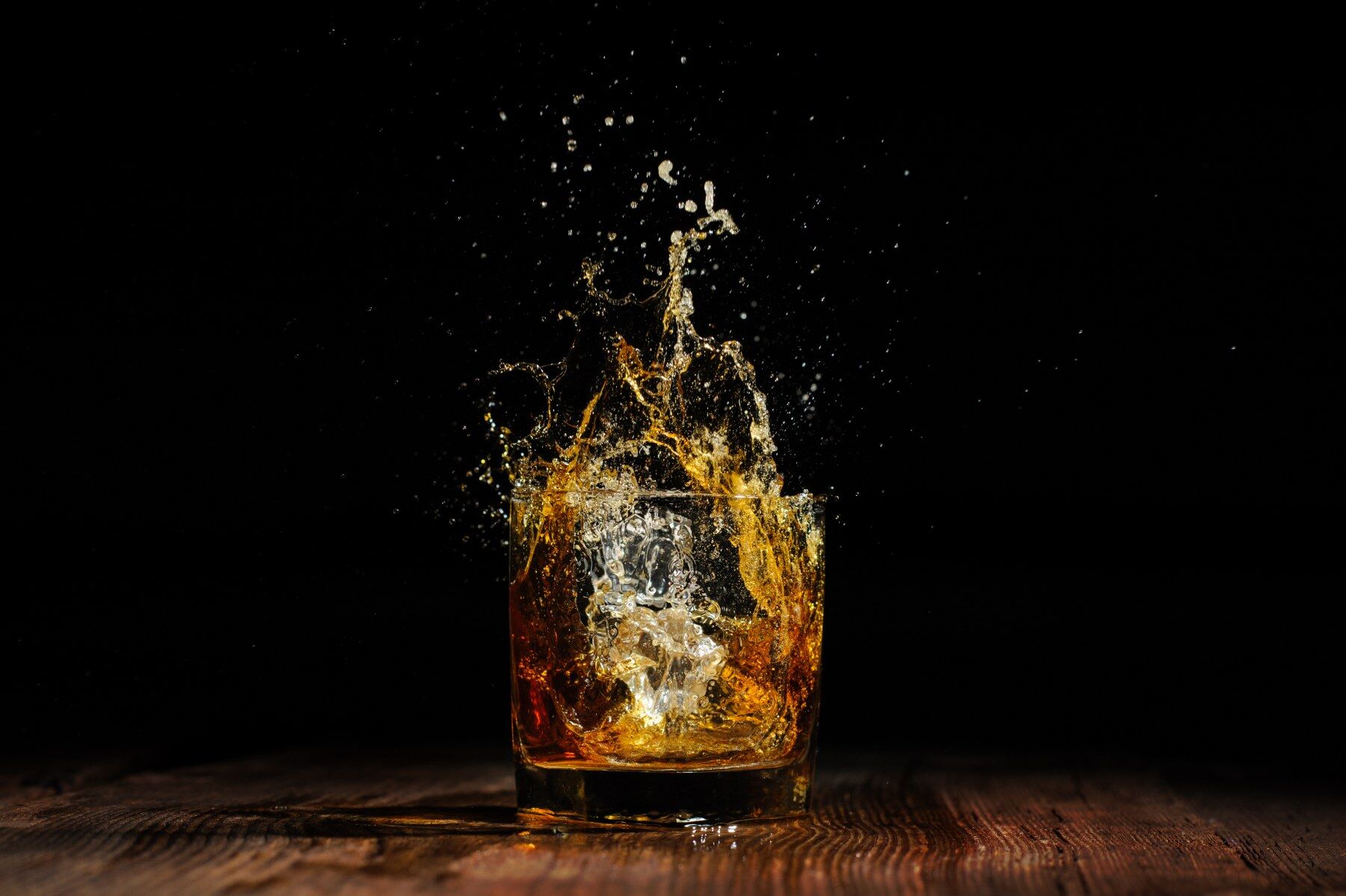 Ice cubes being dropped into a glass of amber coloured liquor and causing a splash