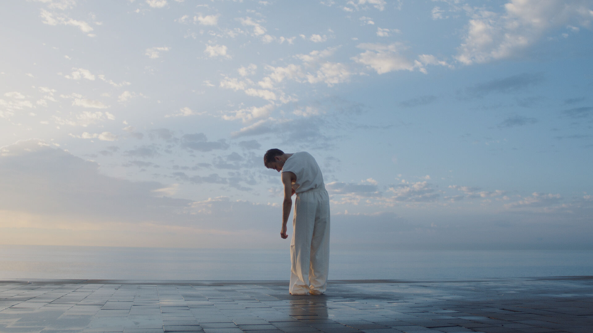 A man stood on a dark, tiled floor at the edge of a big blue sky