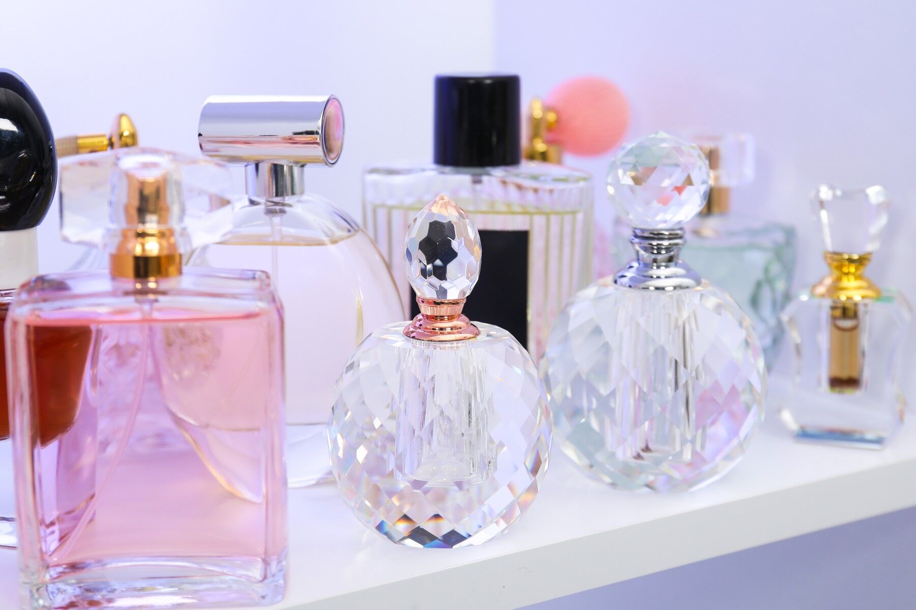 A group of multicoloured perfume bottles on a white shelf