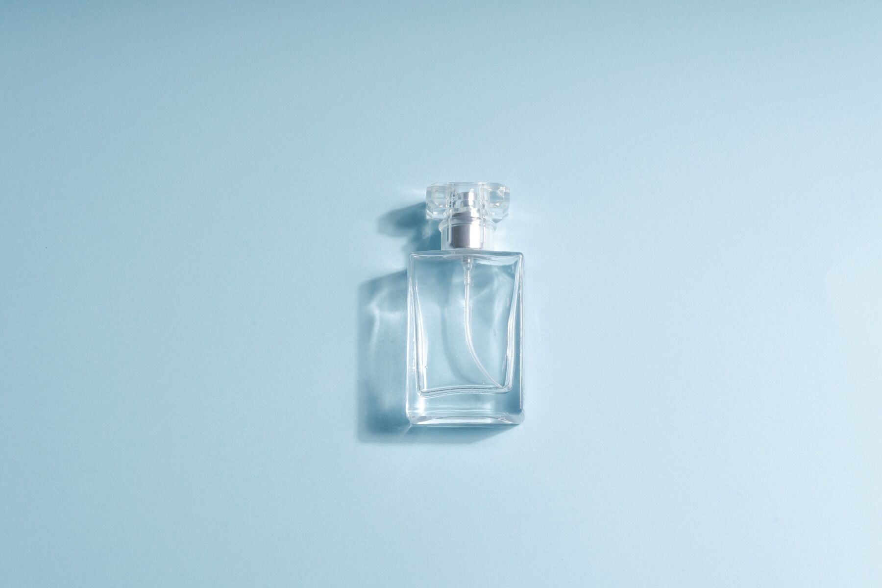 A minimalist image of a plain perfume bottle simply shown on a light blue backdrop