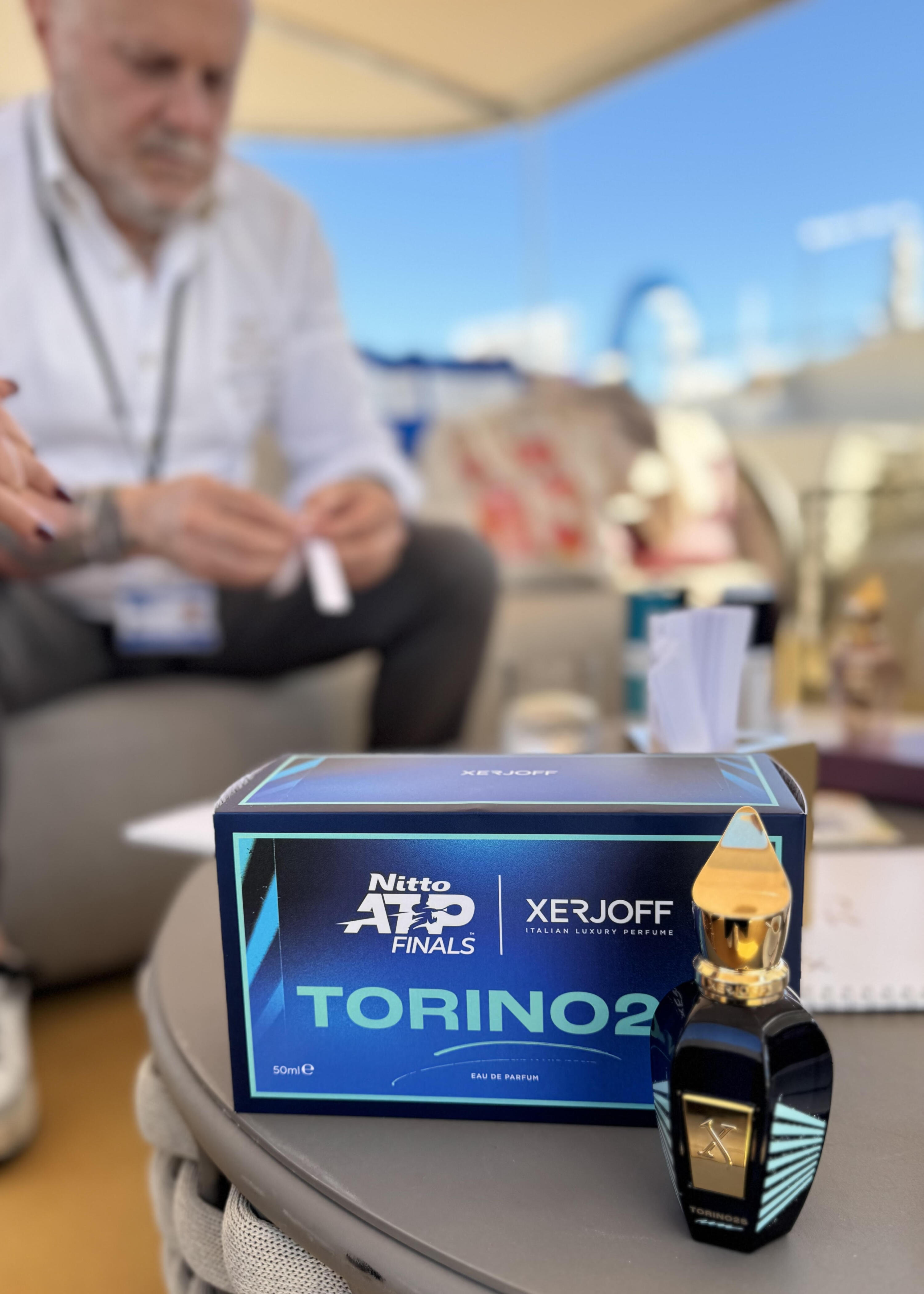 Láhev Torino25 na stole zalitém sluncem se Sergiem Momem v rozostřeném pozadí