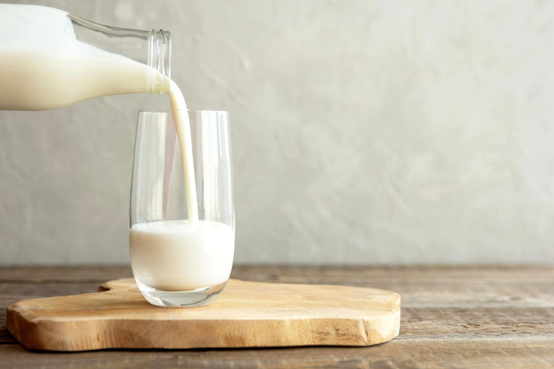 A bottle of milk pouring into a glass on a table