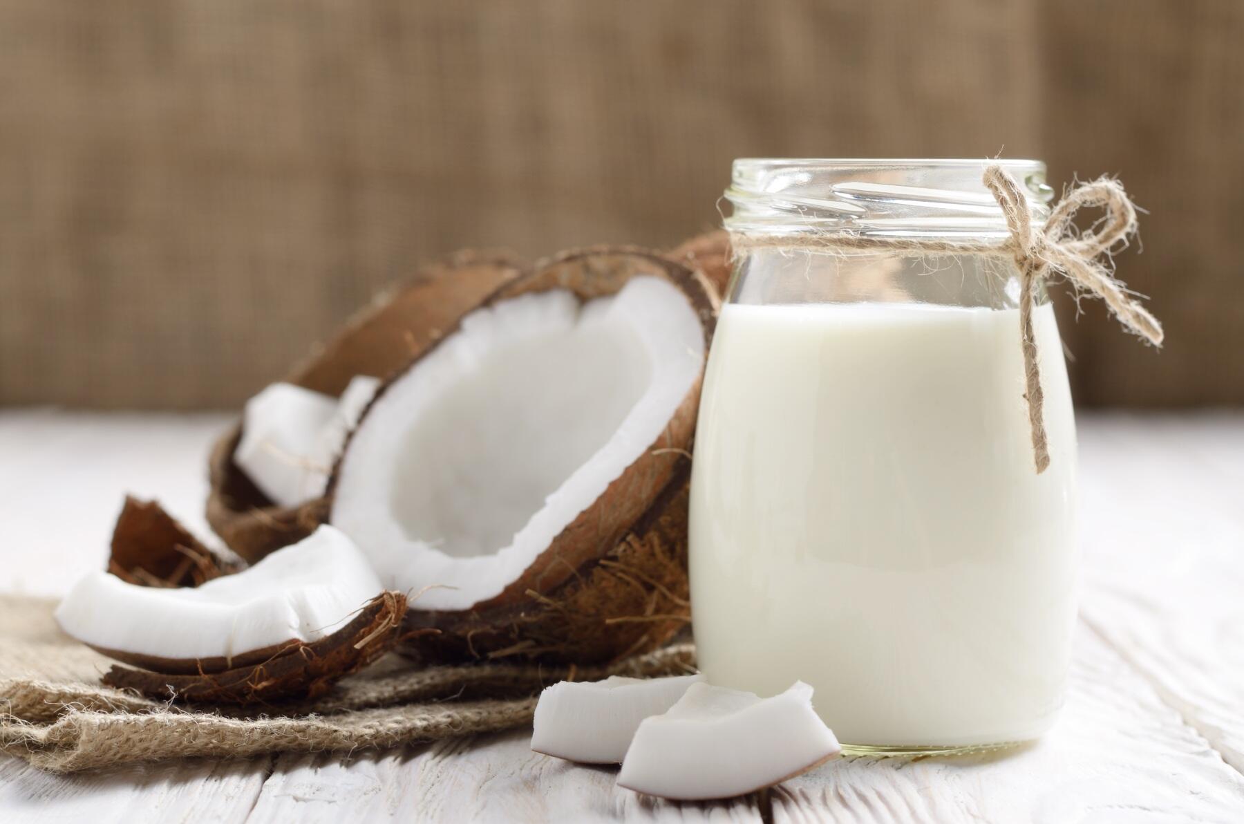 A glass of coconut milk with an open coconut lying beside it