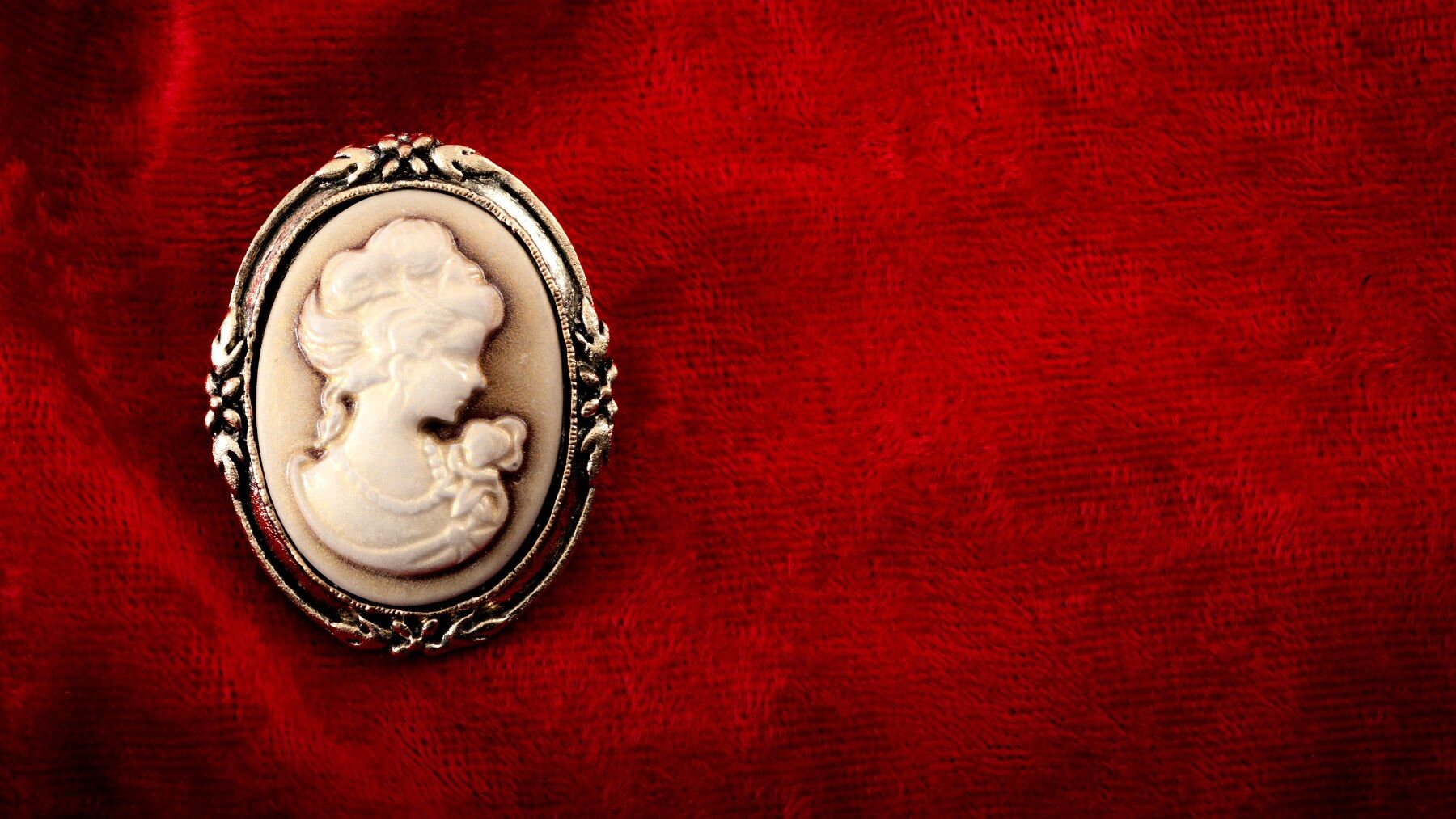 A Victorian style cameo broach laid on a piece of red fabric