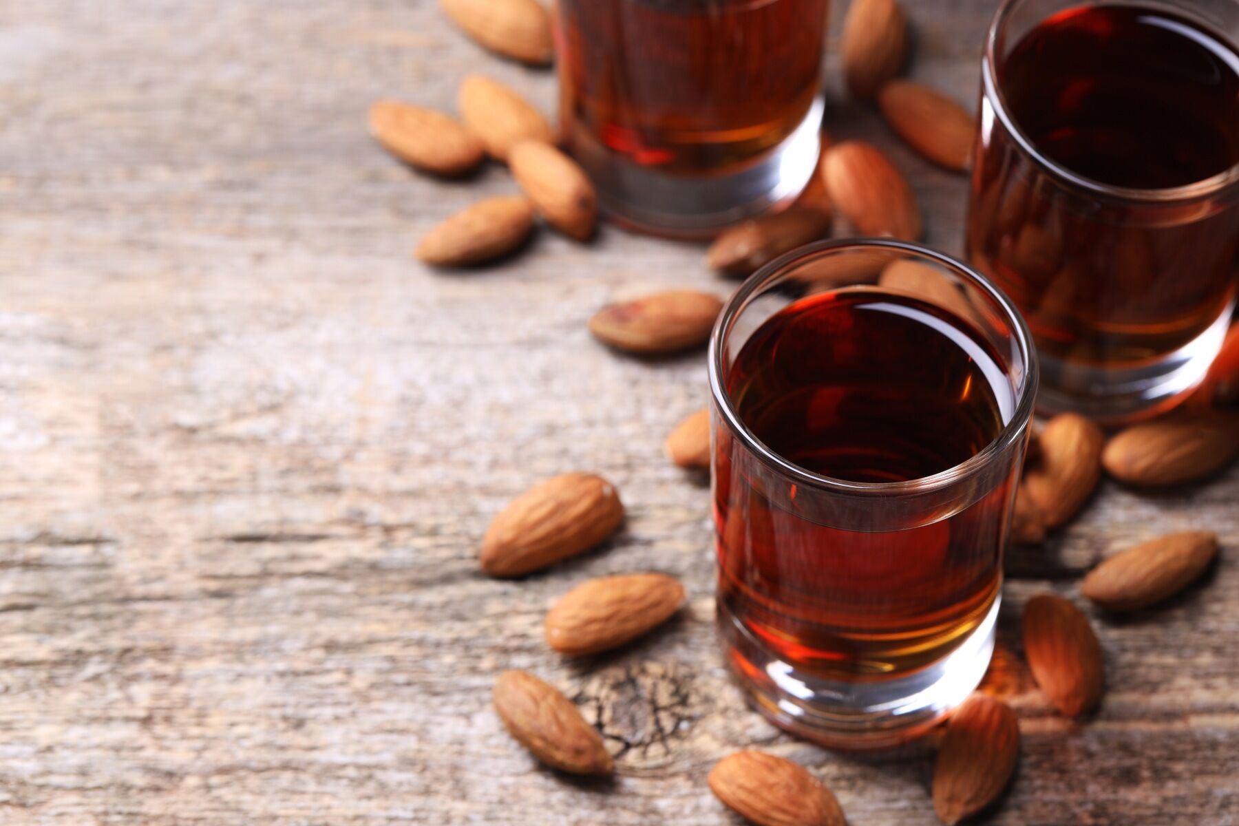 A glass of amaretto liqueur surrounded by almonds