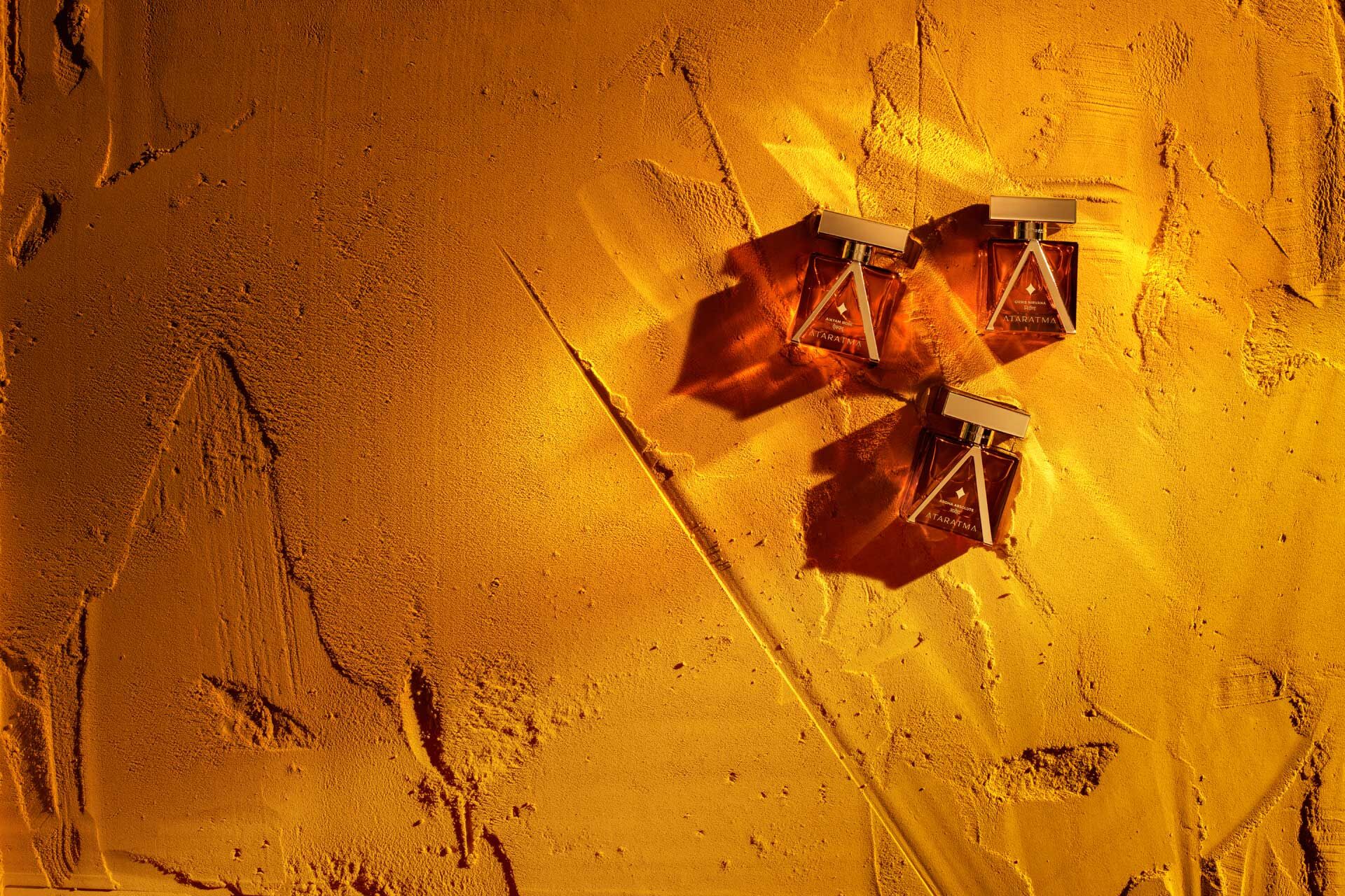 Three of the Ataratma perfumes on sand in golden light