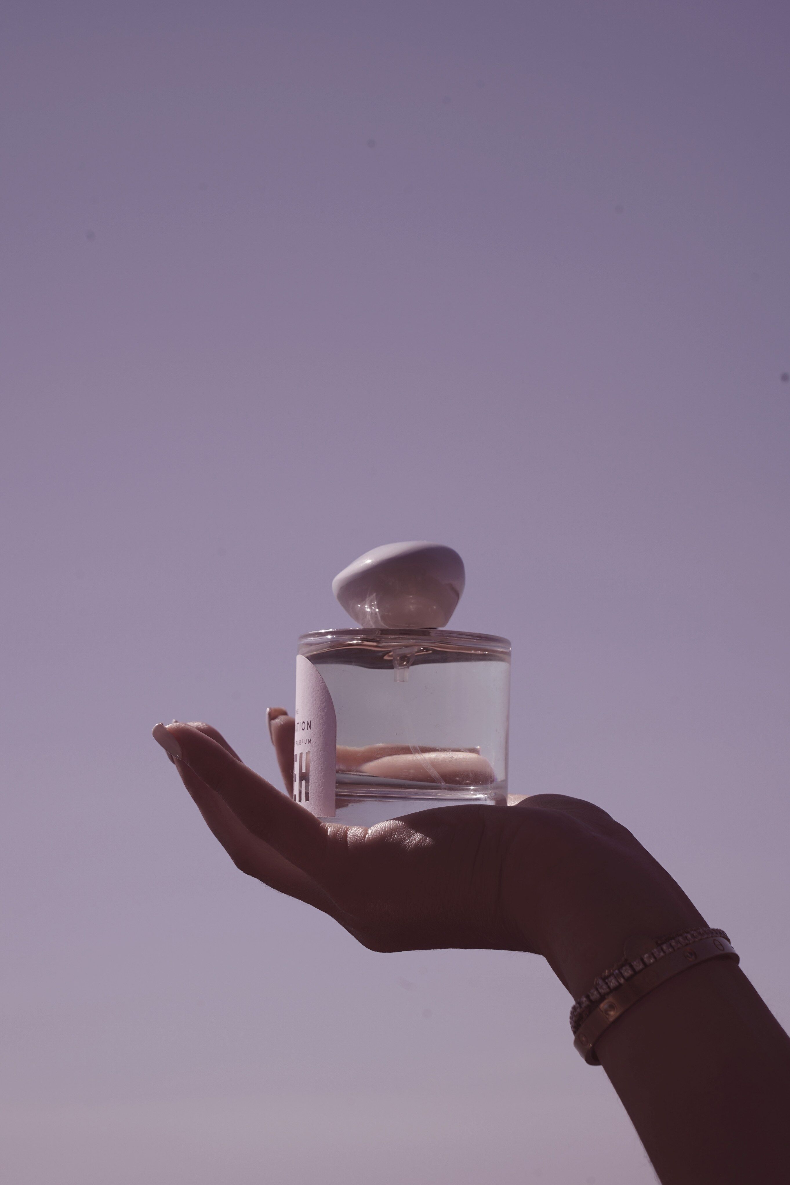 A hand holding a bottle of Neh perfume up to the sky