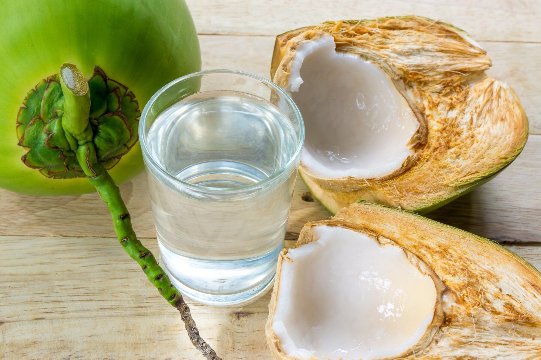 A green coconut split open to show the flesh inside along with a glass of coconut water
