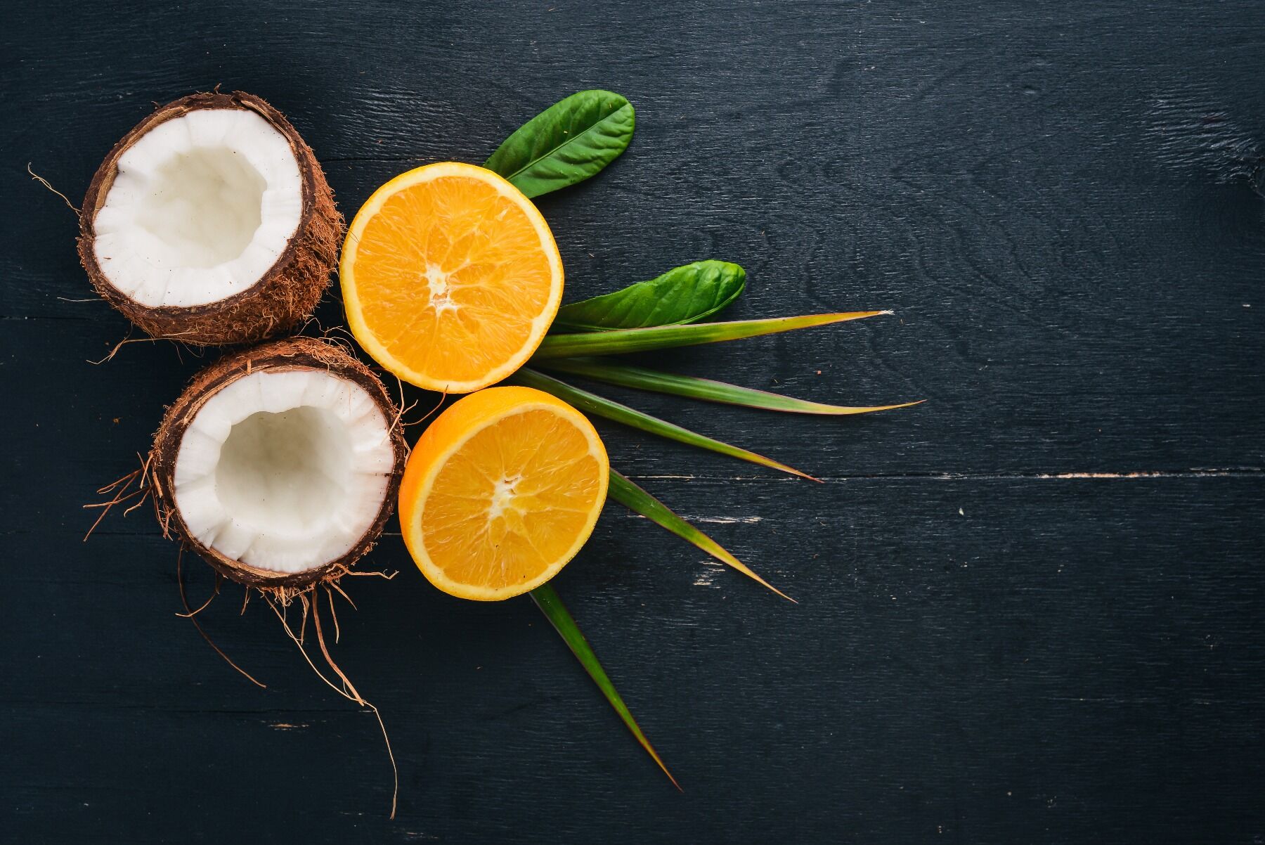 An orange cut in half next to a coconut cut in half, placed on a slate backdrop