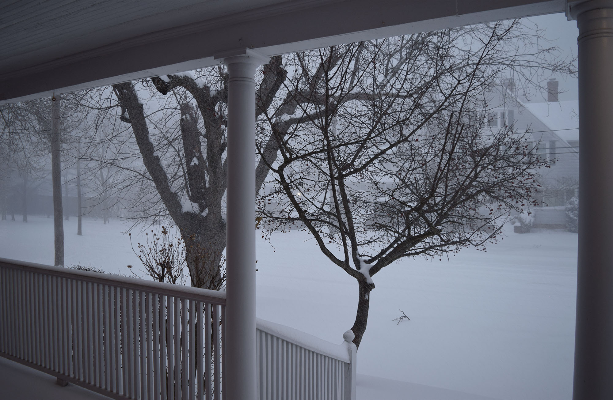 Veranda s výhledem na bílou ulici zapadanou sněhem v zimě.