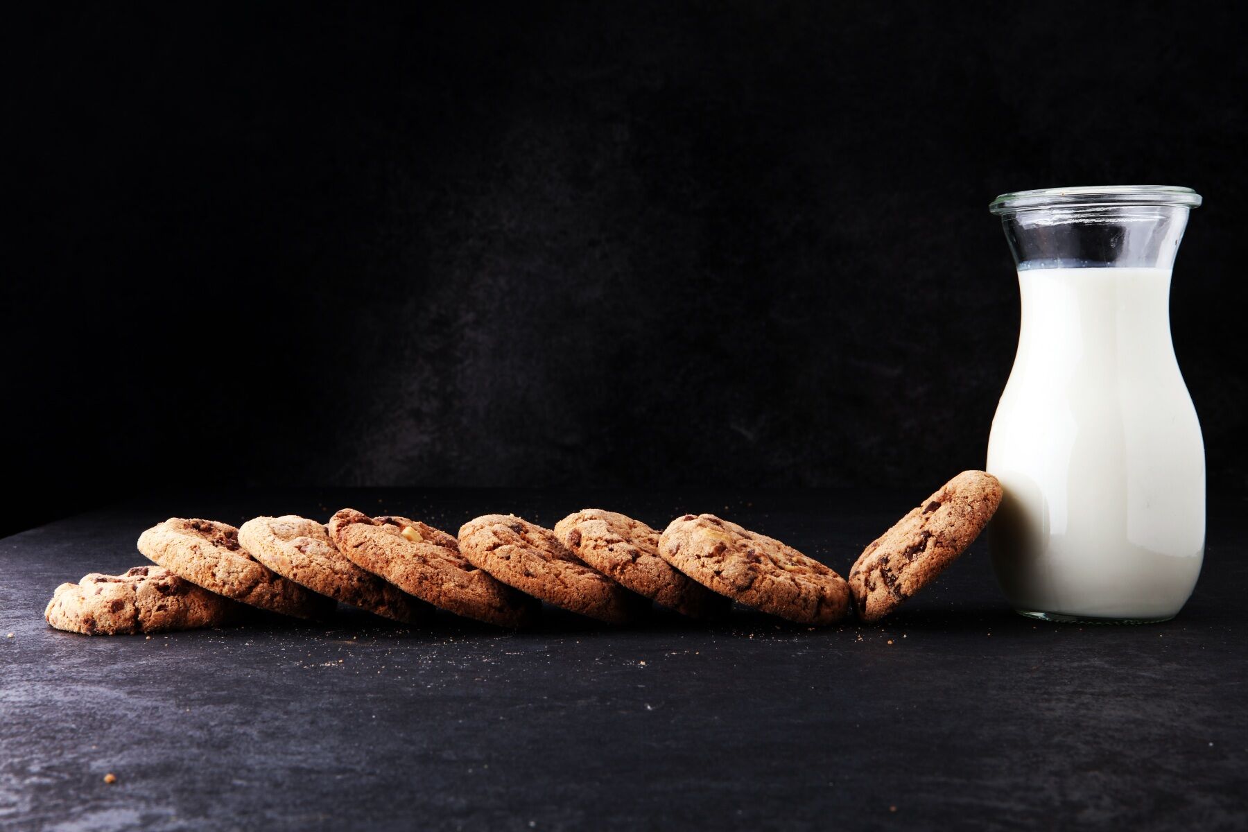 A bottle of milk and a row of cookies placed on a slate