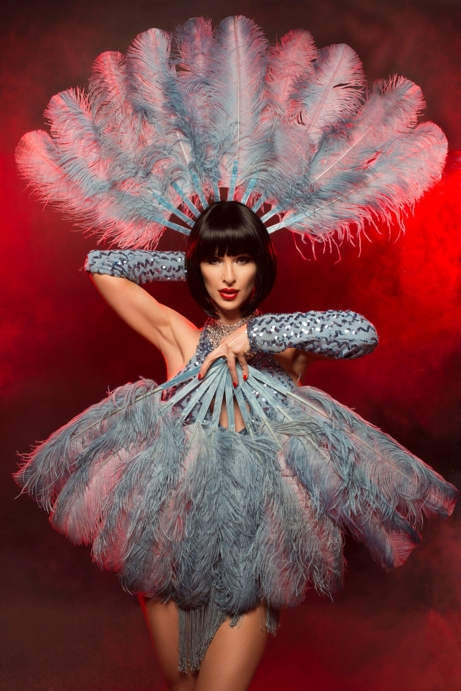 A burlesque dancer dressed in silver holding two fans