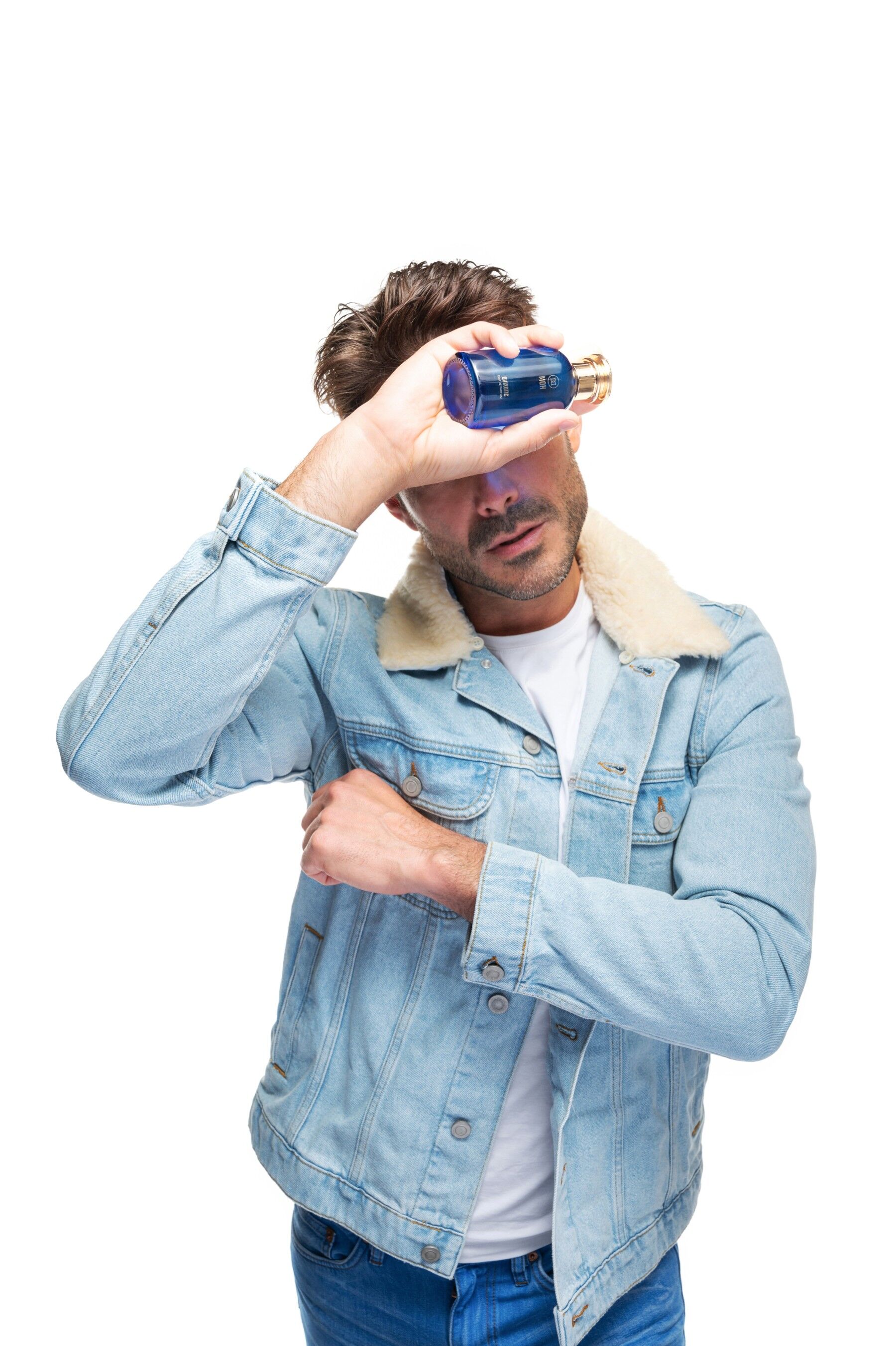 A man dressed in blue tones holding a bottle of Quixotic up to cover his face