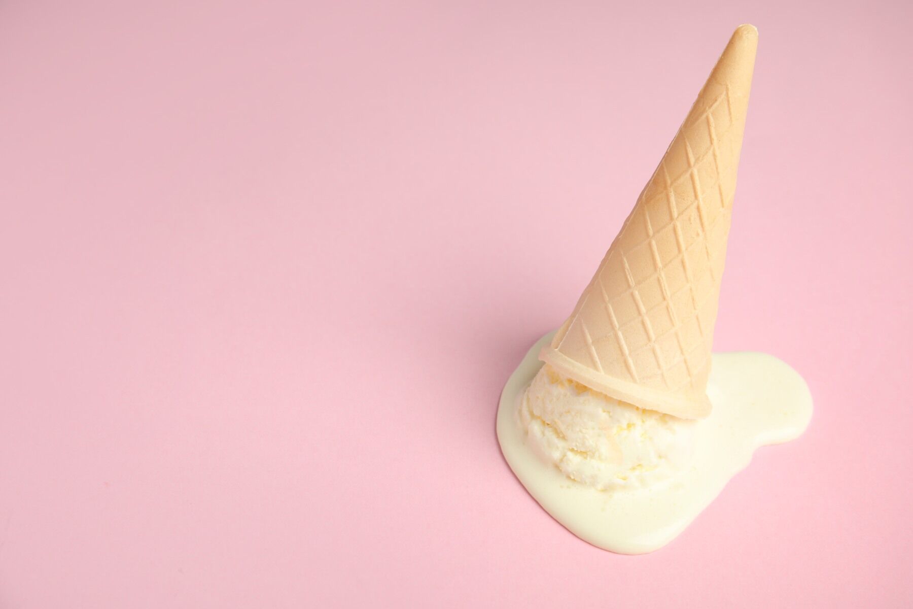 An ice cream that has been dropped and is melting on a pink backdrop