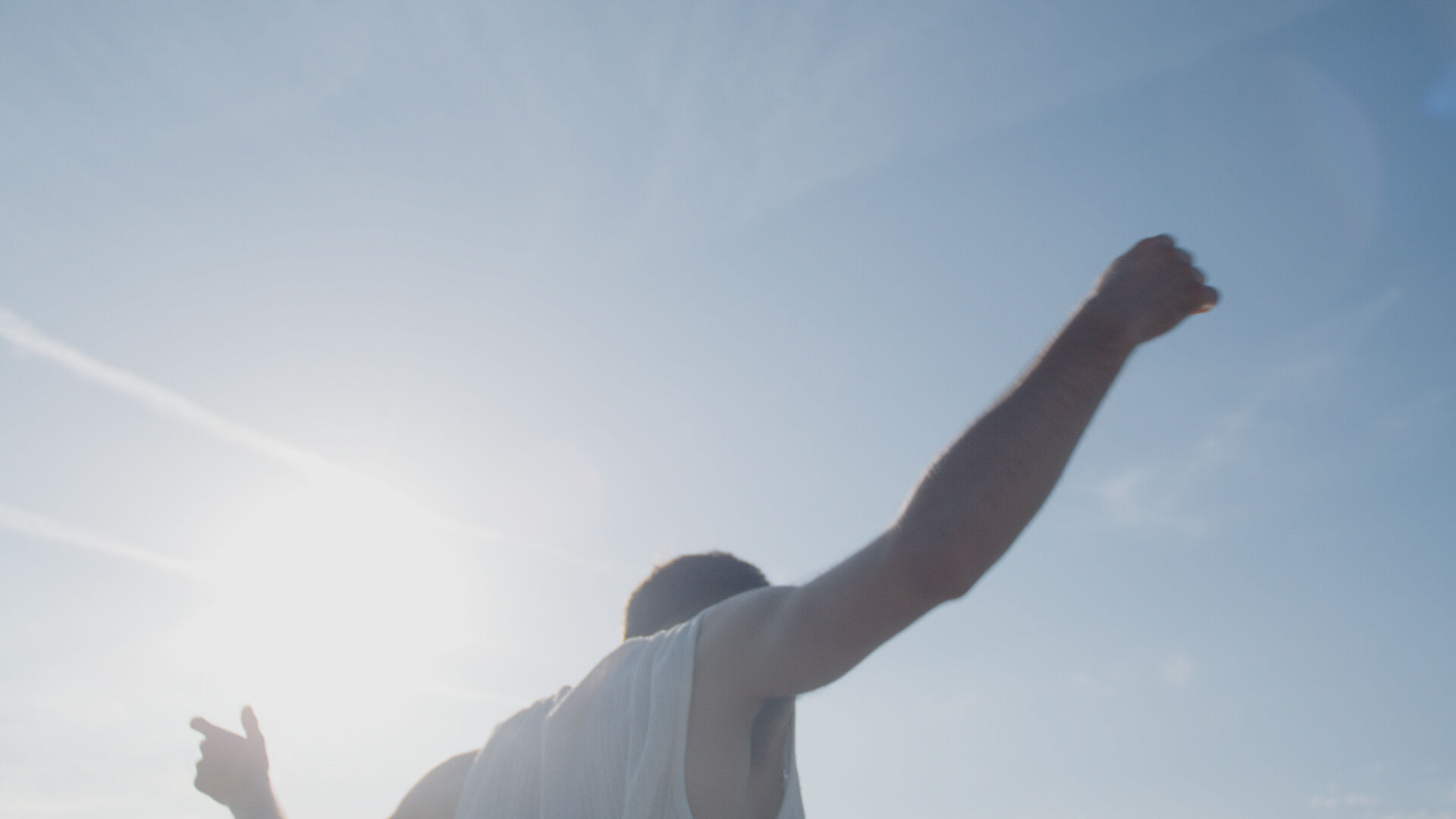 A man throwing his arms in the air against a blue sky