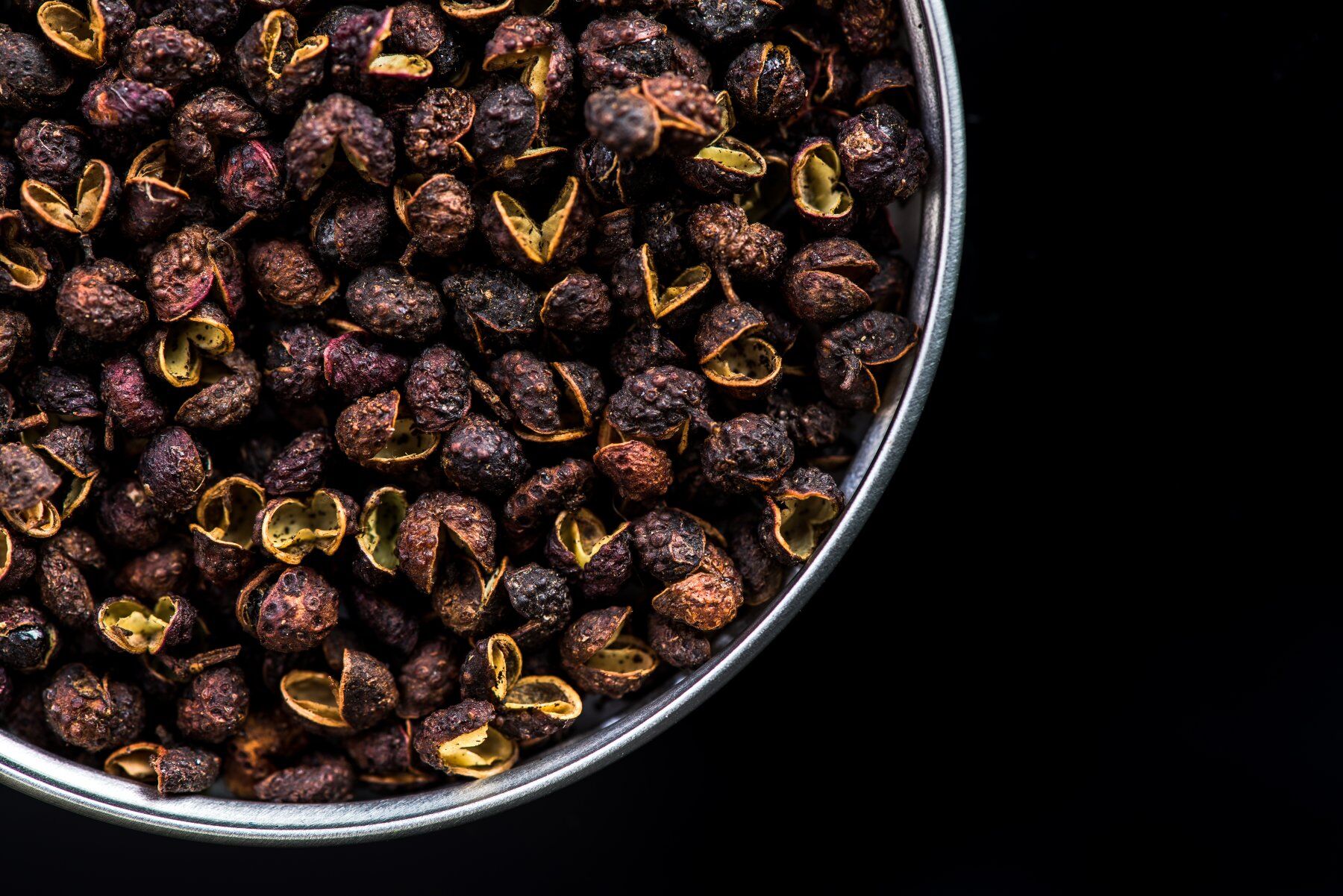 Timur peppercorns in a bowl against a black backdrop
