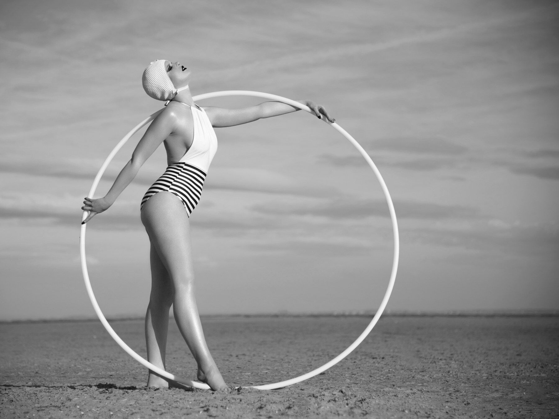 A vintage styled lady with a large hoop wearing a bathing costume posing on the beach