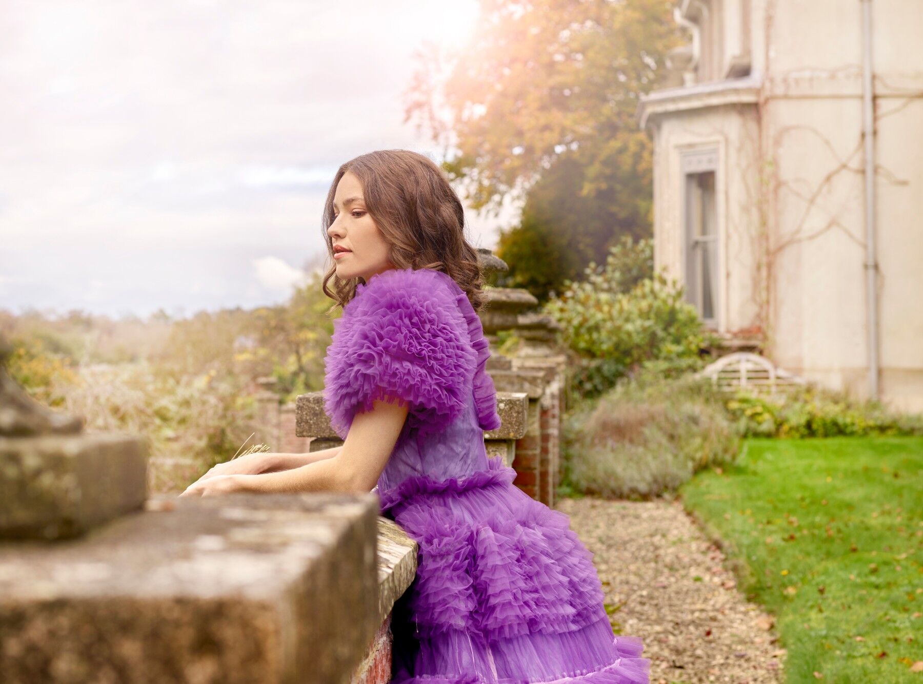 Woman in frothy purple dress looking over the balcony of what appears to be a huge country house