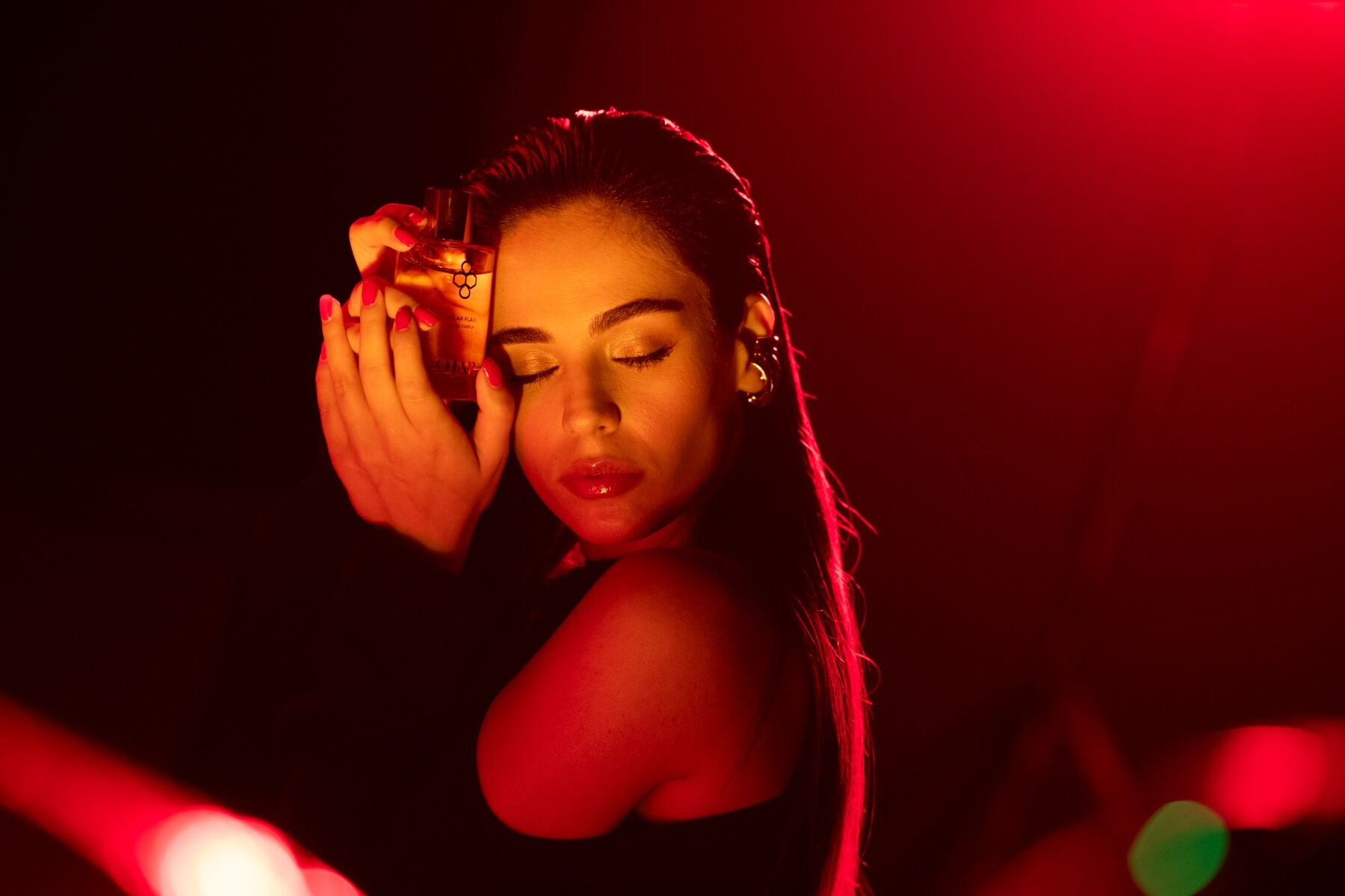 A woman in red light caressing a bottle of perfume